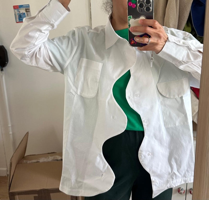 La Chemise Blanche portée ouverte sur un t-shirt vert : patte de boutonnage ondulée et poches asymétriques