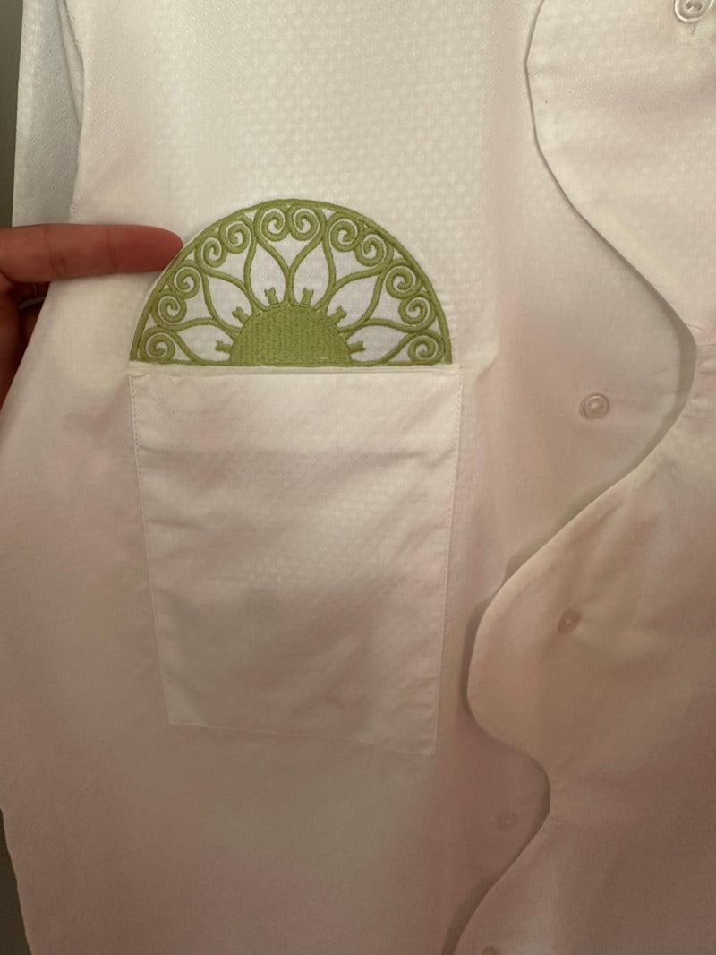 Détail d’une poche et d’une broderie soleil vert, motif de ferronnerie, sur le jacquard blanc