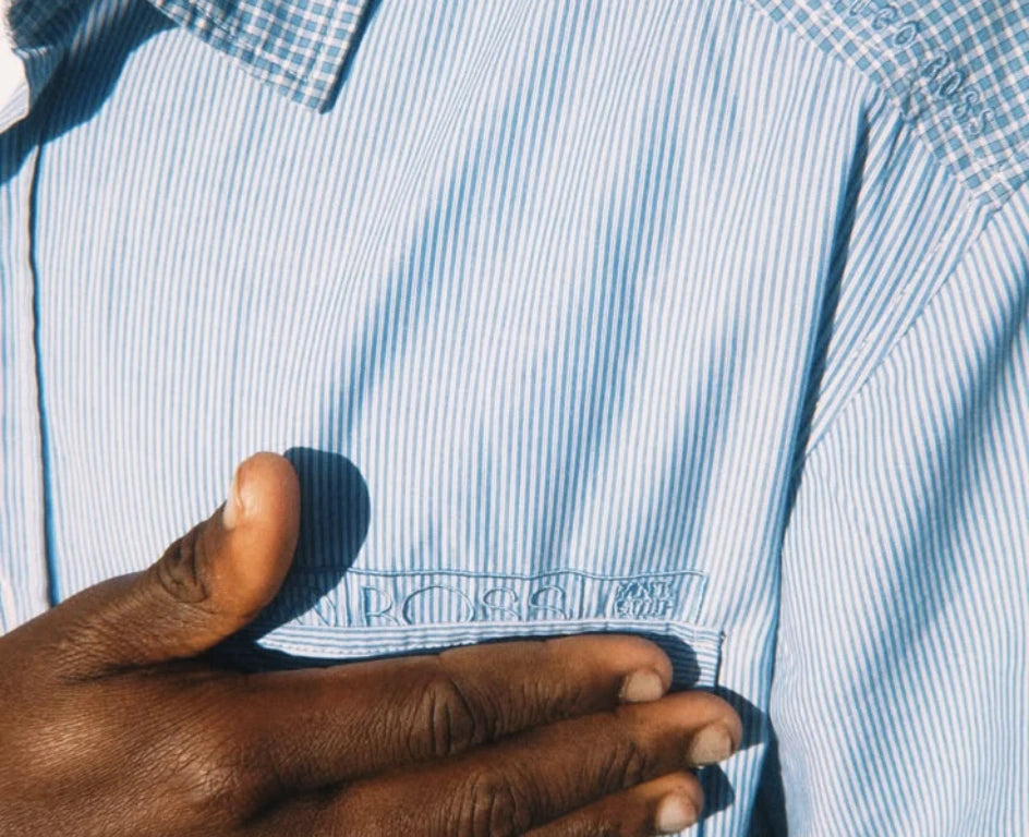 Une main posée sur une chemise rayée bleue, au soleil
